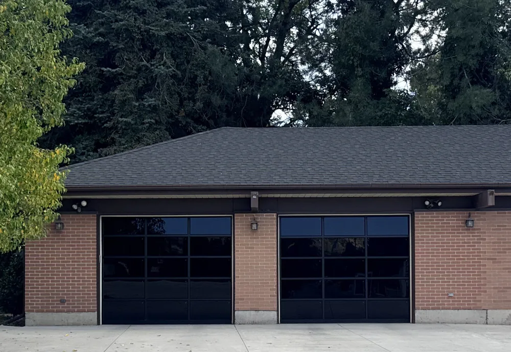 Two black full-view glass garage doors installed on a brick garage in Utah