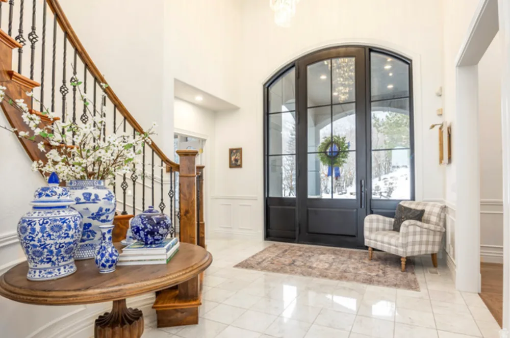 Bright foyer with a staircase and arched black iron double doors, seen from inside