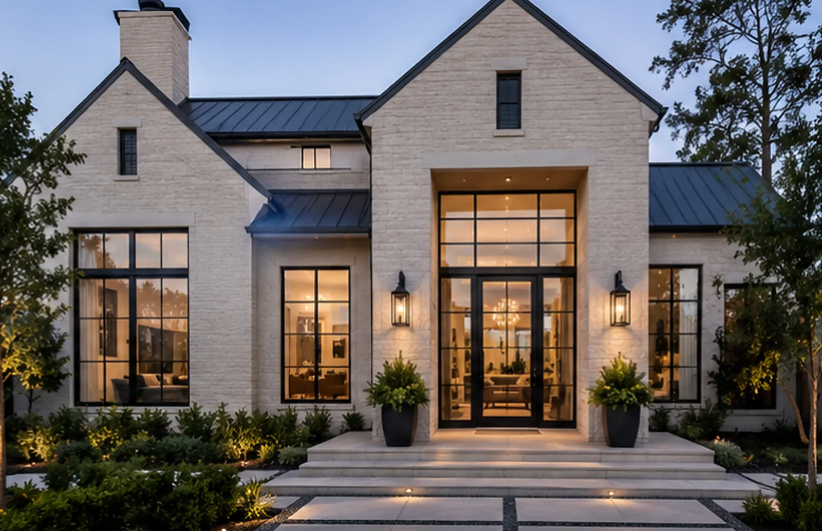 Limestone home at dusk with black steel grid windows and a tall steel-and-glass entry